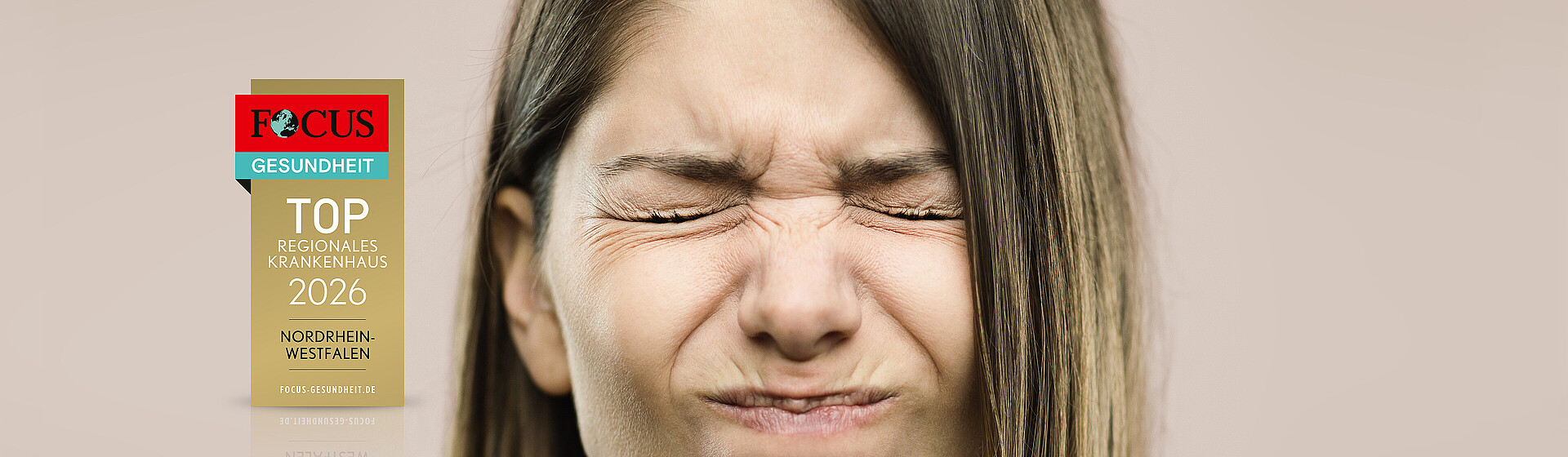 Frau mit schmerzverzerrtem Gesichtsausdruck, mit einem Focus-Gesundheit-Siegel für "TOP regionales Krankenhaus"
